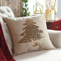 a christmas tree pillow sitting on top of a white couch next to a red blanket