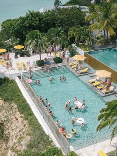 an aerial view of people in a swimming pool surrounded by palm trees and umbrellas