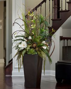 a vase filled with flowers sitting on top of a wooden floor next to a stair case