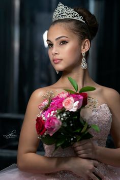 a beautiful young woman wearing a tiara and holding a bouquet of flowers in her hands