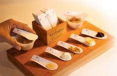 a wooden tray topped with bowls and spoons filled with different types of condiments