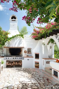 an outdoor kitchen with white walls and stone flooring, covered in pink bougaia