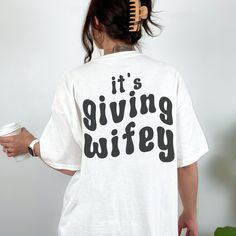 a woman wearing a white t - shirt with the words it's giving wife printed on it