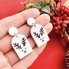 two white earrings with black and red designs on them sitting in front of a plant