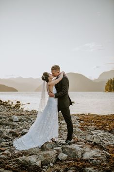 a bride and groom kissing on the rocks by the water at their mountain wedding in british columbia