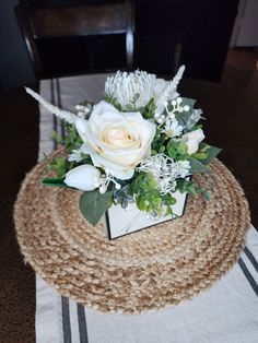 a white flower arrangement sitting on top of a placemat in front of a table