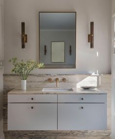 a bathroom with marble counter tops and white cabinets, along with a large mirror above the sink