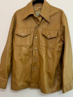 Vintage 1970s  faux leather coat/shacket made by Pacific Trail. The jacket is a camel color with pocket details and silver buttons. In pre-owned condition with some signs of wear (shown in photos) including a few nicks in the material.  Measurements Length 28.75in Chest 42in  Sleeve 20in  Shoulders  21.75 Retro Brown Outerwear With Snap Buttons, Vintage Button-up Leather Jacket With Pockets, Vintage Leather Jacket With Button-up Pockets, Vintage Leather Outerwear With Button Closure, Vintage Brown Outerwear With Double Button Closure, Vintage Brown Single-button Outerwear, Retro Brown Single-breasted Leather Jacket, Vintage Brown Single-breasted Leather Jacket, Faux Leather Coat