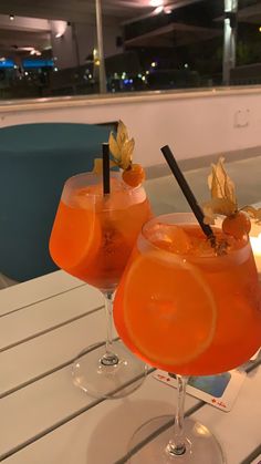 two glasses filled with orange juice and garnished with leaves sit on a table