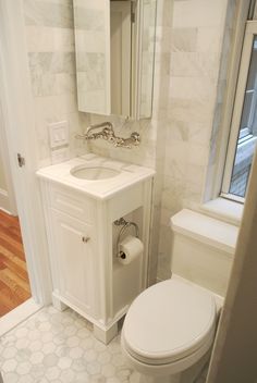 a white toilet sitting next to a sink in a bathroom under a mirror and a window