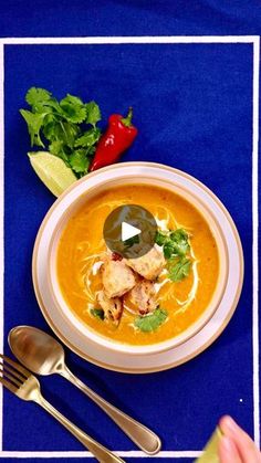 a bowl of soup on a blue place mat with silverware and spoons next to it