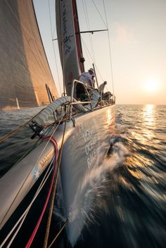 a sailboat sailing in the ocean at sunset with sails down and two people on it