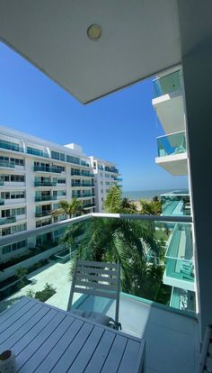 an apartment balcony overlooking the ocean and palm trees in front of it, with white balconies on either side