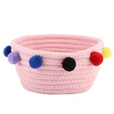 a pink basket with multi colored pom poms on the handles and bottom,