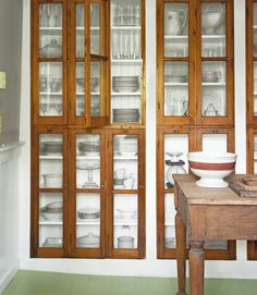 an old wooden table topped with lots of glass doors next to a cabinet filled with dishes