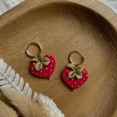 two strawberry shaped key chains sitting on top of a wooden tray next to feather feathers