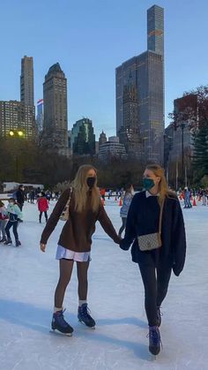 two women are ice skating in the middle of a city park with skyscrapers in the background