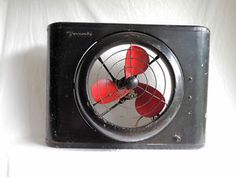 an old style fan sitting on top of a white wall next to a red light