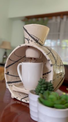 a coffee cup and saucer sitting on a table next to succulents