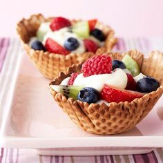 two waffle cups filled with fruit on top of a white plate next to a fork