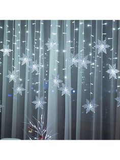 snowflakes are hanging from the curtain in front of a christmas tree with lights