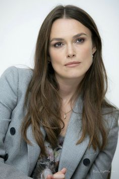 a woman with long brown hair wearing a gray jacket