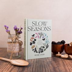 the book slow seasons is next to two wooden bowls and spoons with flowers in them