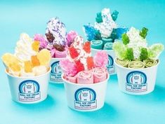 four ice cream cups filled with different colored candies and toppings on blue background