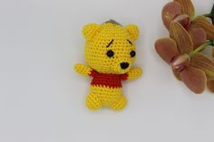 a crocheted winnie the pooh keychain next to a flower