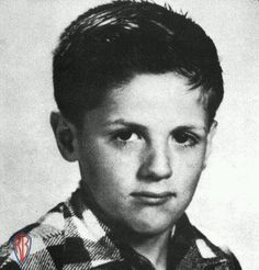 a black and white photo of a young boy with short hair wearing a checkered shirt