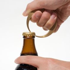 a hand holding a beer bottle with a gold ring on it's top and another hand reaching for the bottle