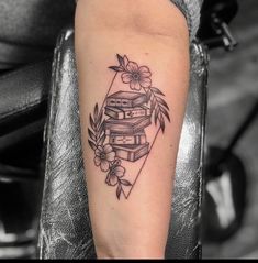 a woman's arm with a stack of books and flowers tattoo on her left forearm