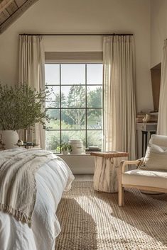 a bed sitting under a window next to a white chair and table in a bedroom