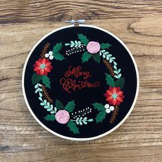 a black embroidered christmas wreath with red and green flowers on the front is sitting on a wooden surface