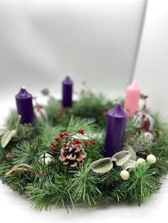 a wreath with purple candles and pine cones on the top, surrounded by greenery