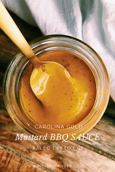 a jar filled with mustard sitting on top of a wooden table next to a spoon