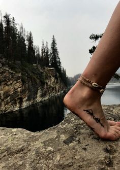 a person standing on top of a rock next to a body of water with trees in the background