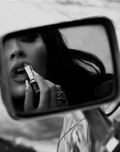 a woman is talking on her cell phone in the side view mirror while she brushes her teeth