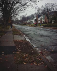 a person walking down the street on a rainy day with houses in the back ground