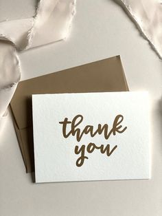 a thank card with the words thank you written on it in brown ink next to an envelope