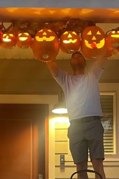 a man is holding up pumpkins with faces carved into them on the ceiling in front of his house