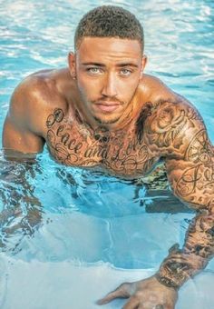 a man in the water with tattoos on his arm and chest, looking at the camera