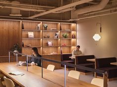 two people are sitting at a table in an office with wooden shelves and shelving