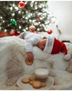 a baby in a santa hat sleeping on a blanket next to cookies