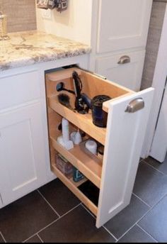 an open cabinet in the middle of a kitchen with white cabinets and marble counter tops