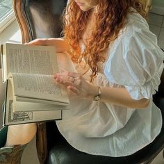 a woman sitting in a chair reading a book with her hands on the open pages