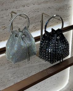 two purses sitting on top of a shelf next to each other, one in black and the other in silver