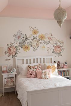 a white bed sitting in a bedroom next to a wall with flowers painted on it