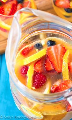 two glasses filled with fruit on top of a blue table next to sliced oranges and strawberries