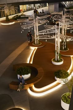 two people sitting on benches in the middle of an open area with lights and plants